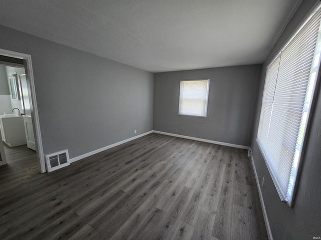 unfurnished room with a sink, baseboards, dark wood-style floors, and visible vents