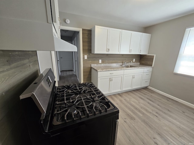 kitchen with stainless steel range with gas cooktop, white cabinetry, a sink, and light wood-type flooring