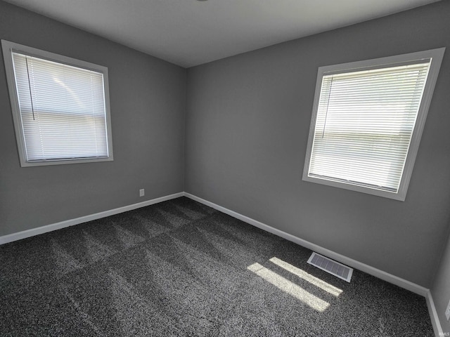 empty room featuring baseboards, dark carpet, and visible vents