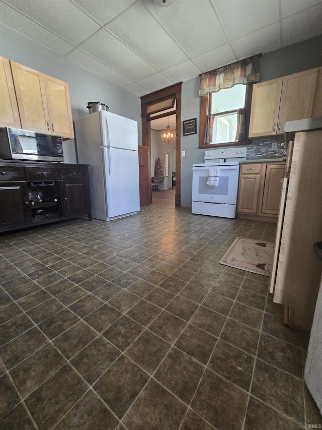 kitchen featuring light brown cabinetry, dark countertops, white appliances, a paneled ceiling, and a chandelier