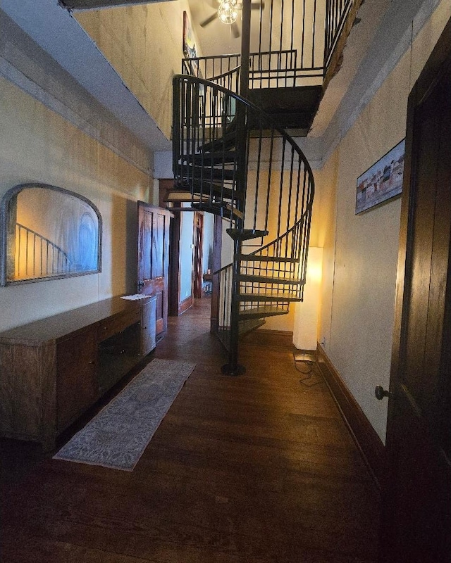 stairway featuring baseboards, ceiling fan, wood finished floors, and a towering ceiling