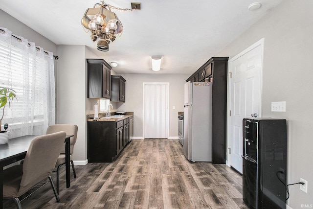 kitchen with a sink, light countertops, freestanding refrigerator, a notable chandelier, and dark wood-type flooring