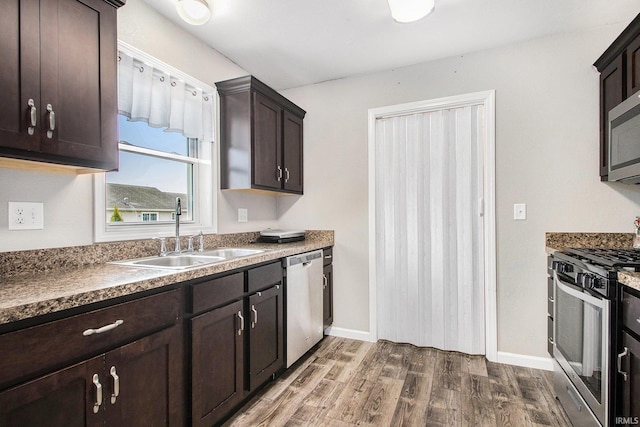 kitchen featuring dark wood-style flooring, appliances with stainless steel finishes, dark brown cabinets, a sink, and baseboards