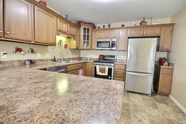 kitchen featuring brown cabinetry, a sink, appliances with stainless steel finishes, and glass insert cabinets