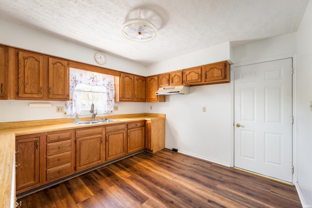 208 E Hickory Grove Rd, Hartford City, IN 47348 - kitchen featuring brown cabinetry, a textured ceiling, under cabinet range hood, a sink, and dark wood finished floors