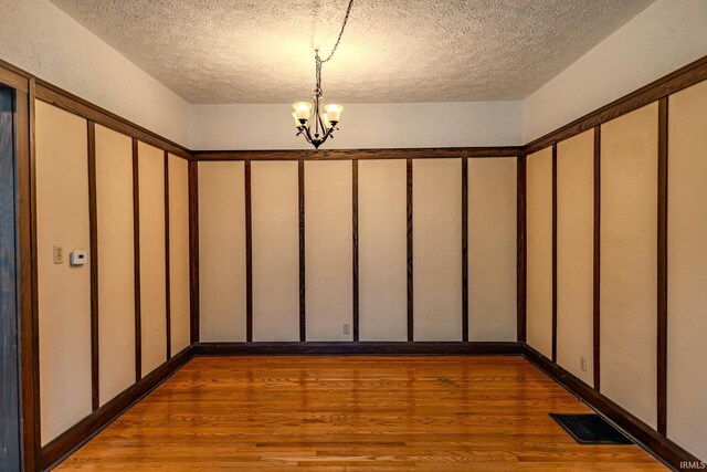 interior space featuring a textured ceiling, a notable chandelier, visible vents, and wood finished floors