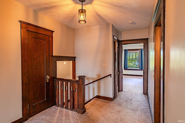 hall featuring carpet floors, a textured ceiling, baseboards, and an upstairs landing