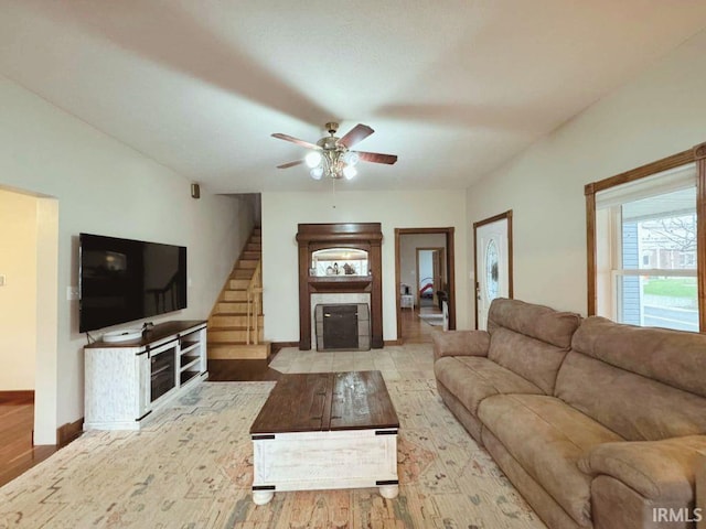 living area with stairs, wood finished floors, baseboards, ceiling fan, and a fireplace with flush hearth