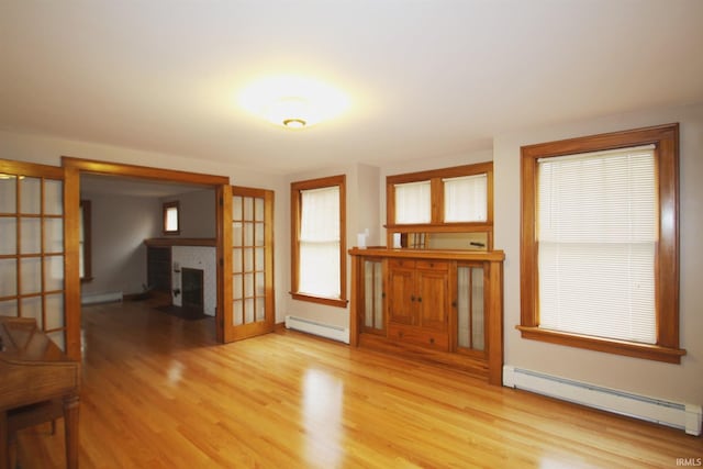 unfurnished living room with french doors, light wood finished floors, and a baseboard radiator