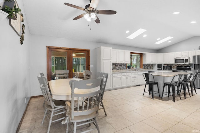 dining room featuring a ceiling fan, baseboards, lofted ceiling with skylight, recessed lighting, and light tile patterned flooring