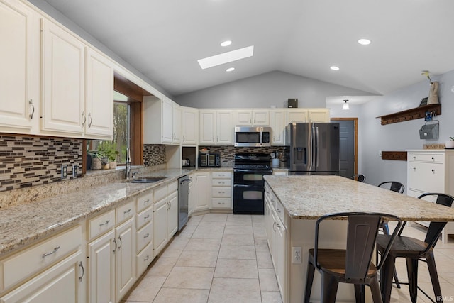 kitchen featuring decorative backsplash, a breakfast bar area, a sink, lofted ceiling with skylight, and stainless steel appliances