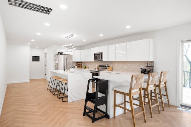 13440 N Summerhill Dr, Albany, IN 47320 - kitchen featuring visible vents, a kitchen breakfast bar, white cabinetry, tasteful backsplash, and stainless steel appliances