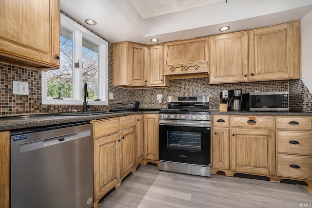 kitchen featuring dark countertops, appliances with stainless steel finishes, a sink, and light wood-style floors