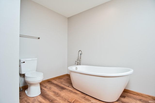 full bathroom with baseboards, toilet, a freestanding tub, and wood finished floors