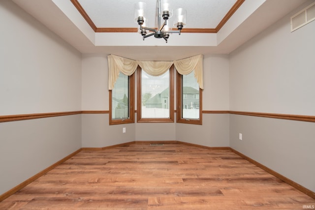 spare room featuring light wood finished floors, a chandelier, a tray ceiling, visible vents, and ornamental molding