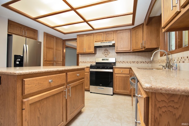 kitchen with brown cabinetry, decorative backsplash, under cabinet range hood, a sink, and stainless steel appliances
