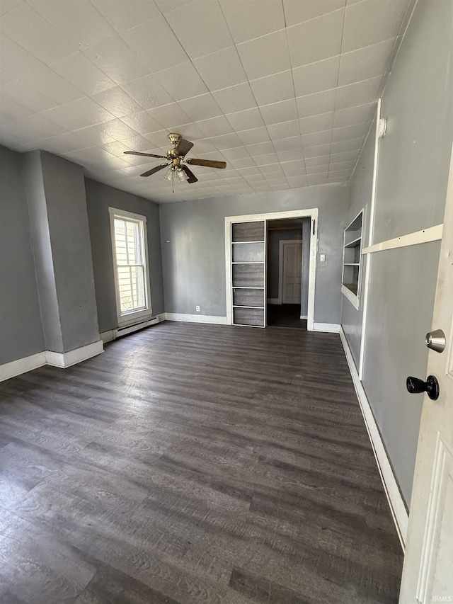 spare room with baseboard heating, baseboards, dark wood finished floors, and ceiling fan