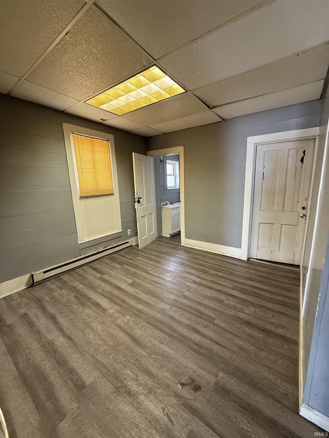 unfurnished room featuring baseboards, baseboard heating, wood finished floors, and a paneled ceiling