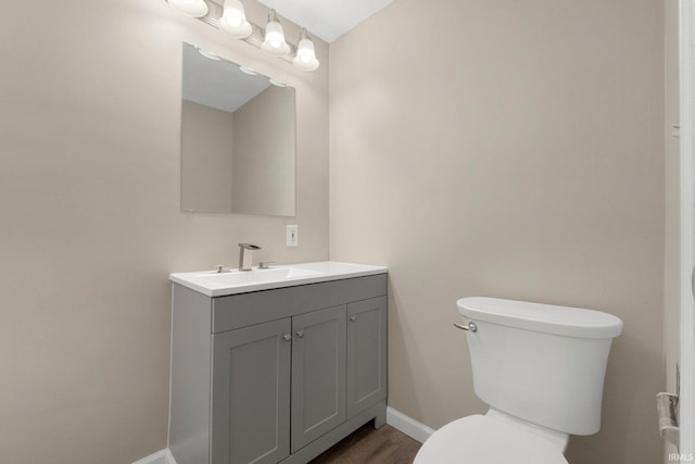 half bathroom featuring vanity, baseboards, toilet, and wood finished floors