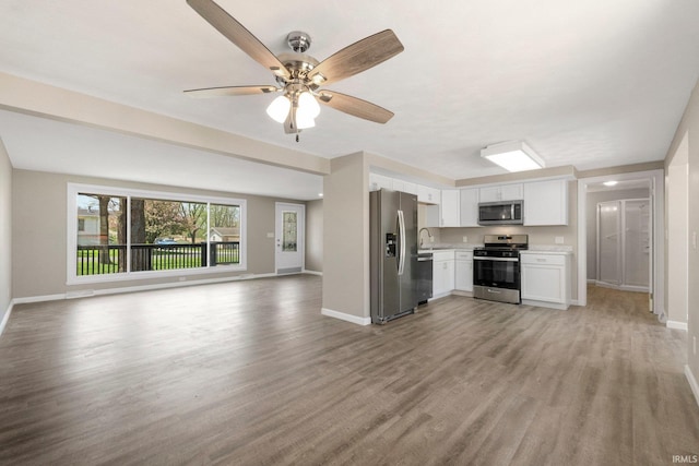 kitchen featuring a sink, light countertops, stainless steel appliances, open floor plan, and white cabinetry