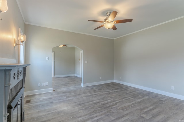 unfurnished room with ceiling fan, arched walkways, a fireplace, baseboards, and light wood-style flooring