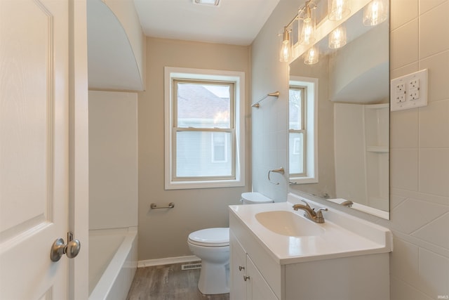 bathroom featuring vanity, toilet, a tub, wood finished floors, and visible vents