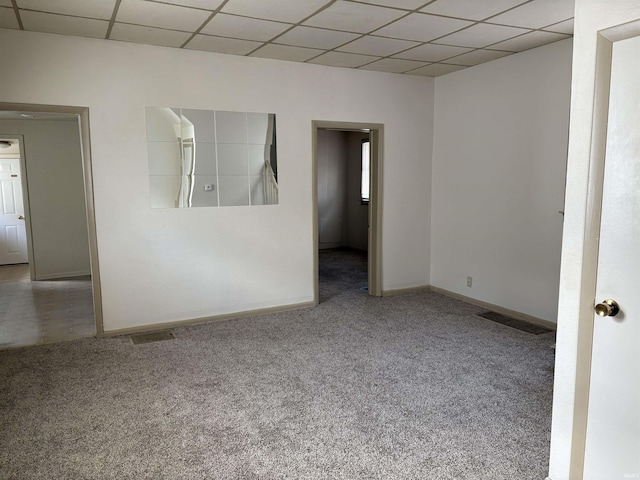 carpeted spare room with baseboards, visible vents, and a drop ceiling