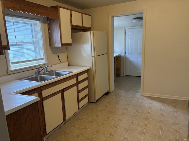 kitchen featuring a sink, light countertops, freestanding refrigerator, light floors, and white cabinetry