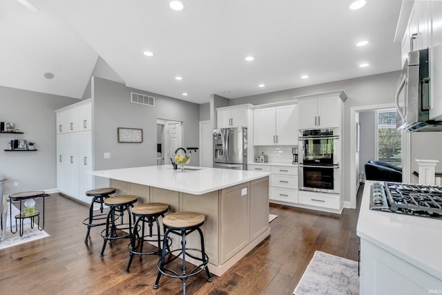 kitchen featuring light countertops, dark wood finished floors, stainless steel appliances, visible vents, and a center island with sink
