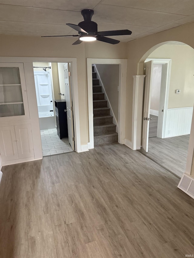 unfurnished living room with arched walkways, a ceiling fan, stairs, and wood finished floors