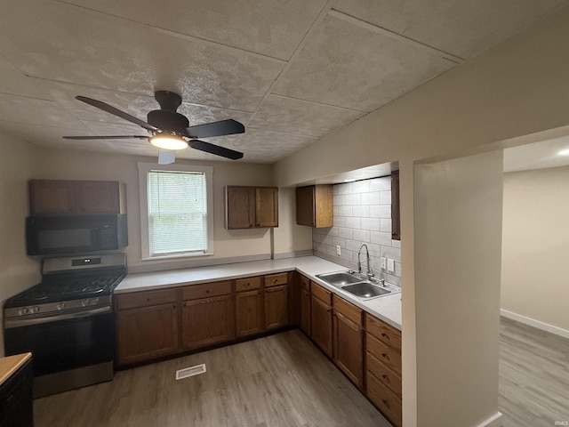 kitchen with black microwave, stainless steel gas range oven, brown cabinets, a sink, and light wood-style flooring