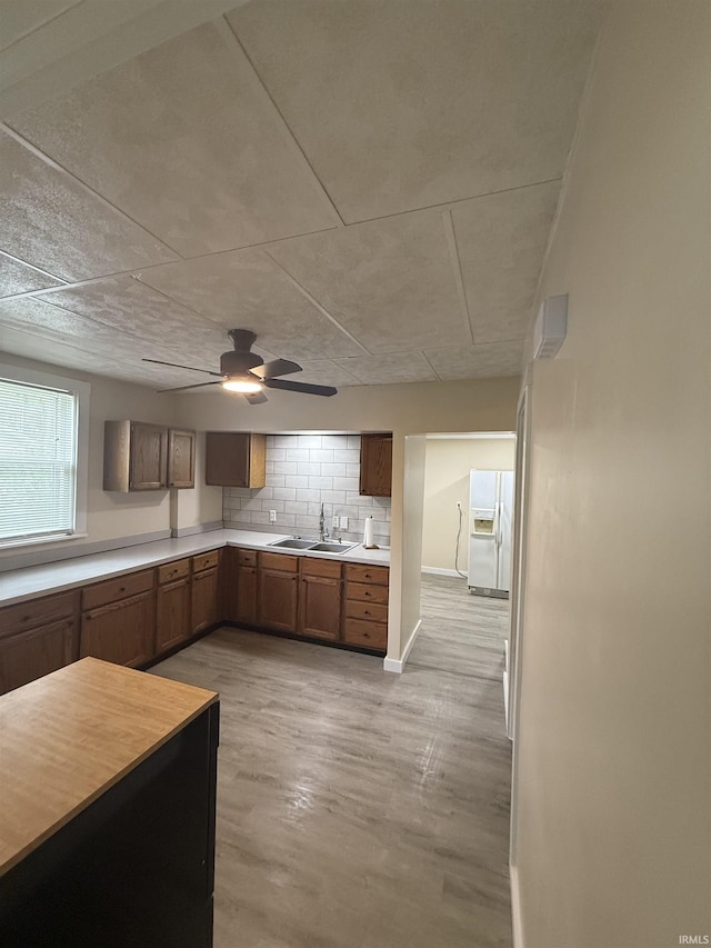 kitchen with baseboards, ceiling fan, light countertops, a sink, and white fridge with ice dispenser