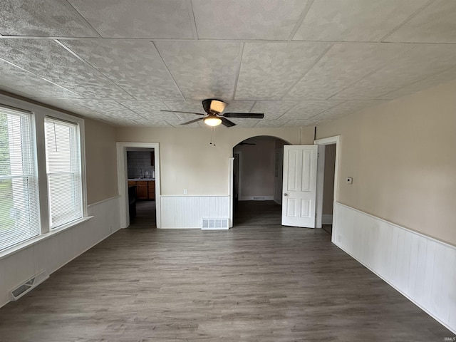 spare room featuring visible vents, arched walkways, ceiling fan, and a wainscoted wall