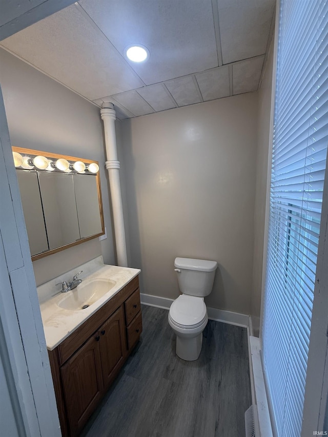 half bath featuring vanity, baseboards, toilet, and wood finished floors