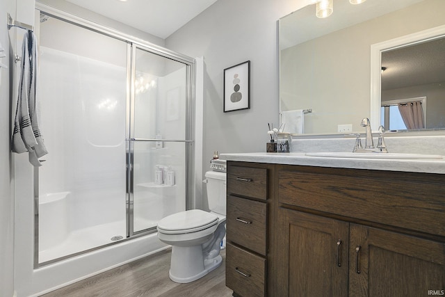 bathroom featuring vanity, toilet, wood finished floors, and a stall shower