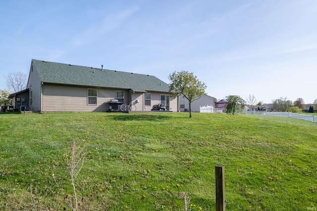 rear view of house with a lawn, fence, and a shingled roof