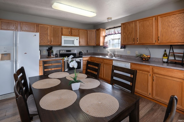 kitchen featuring a sink, dark wood finished floors, brown cabinets, and white appliances