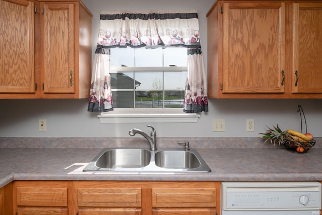 kitchen with brown cabinetry, white dishwasher, and a sink