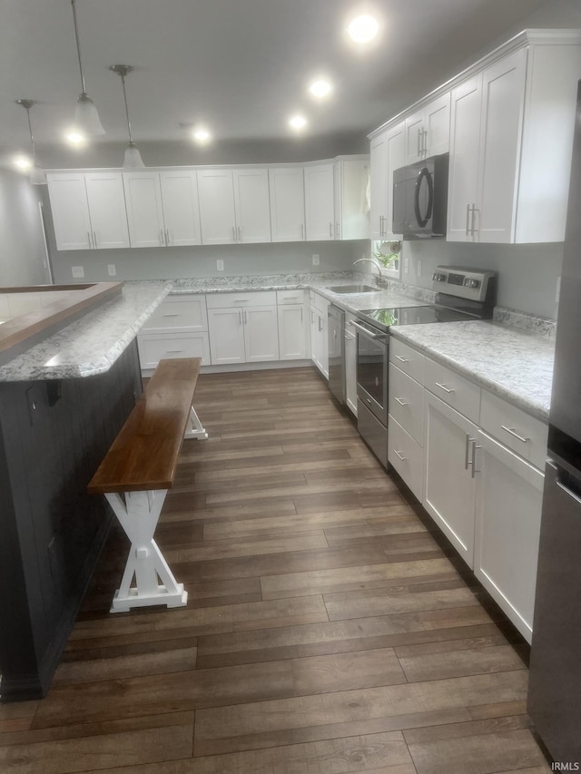 kitchen featuring hanging light fixtures, a sink, white cabinets, stainless steel appliances, and dark wood-type flooring
