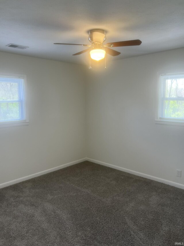 empty room featuring baseboards, a wealth of natural light, dark carpet, and visible vents