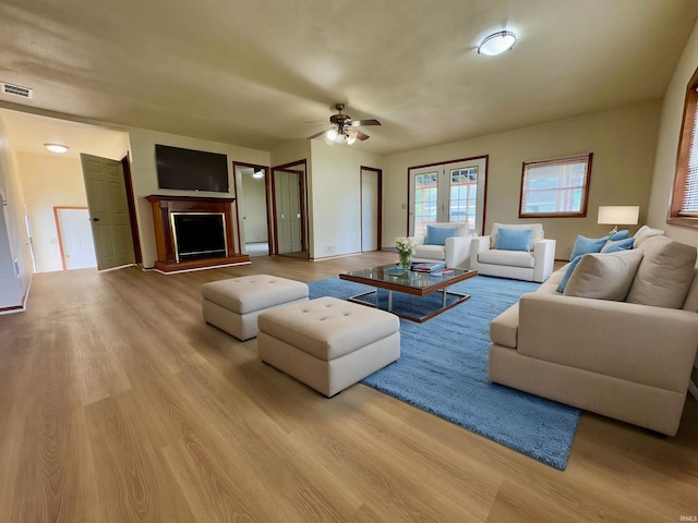 living area with ceiling fan, a fireplace with raised hearth, wood finished floors, and visible vents