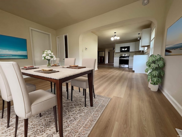 dining space featuring baseboards, arched walkways, and light wood-style flooring