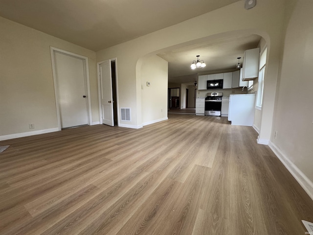 unfurnished living room featuring visible vents, arched walkways, baseboards, and wood finished floors