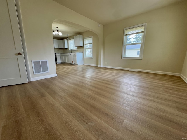 unfurnished living room with visible vents, arched walkways, baseboards, light wood finished floors, and an inviting chandelier