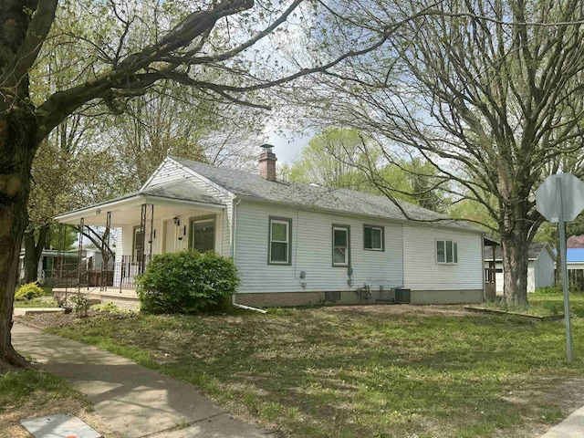 view of front of home featuring a porch, cooling unit, a chimney, and a front lawn