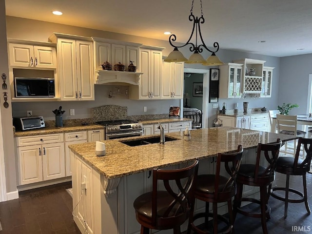 kitchen featuring light stone countertops, a breakfast bar area, a center island with sink, gas range, and a sink