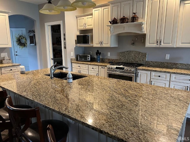 kitchen with stone counters, stainless steel appliances, white cabinetry, and a sink