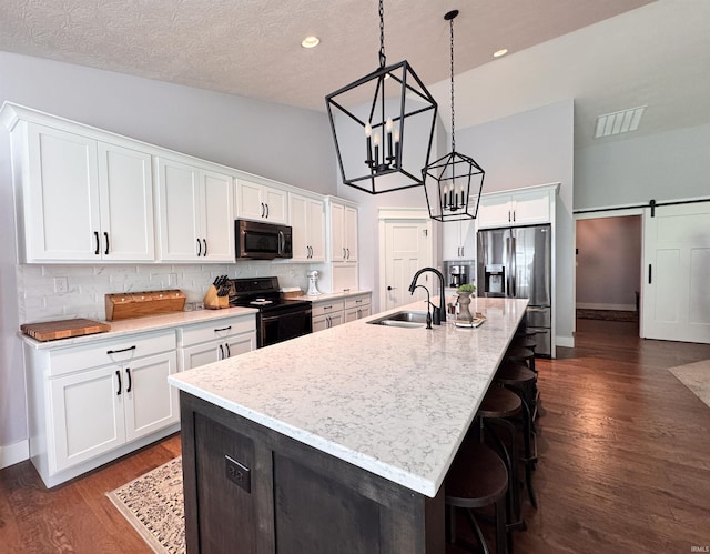 kitchen featuring visible vents, an island with sink, a chandelier, a sink, and black appliances