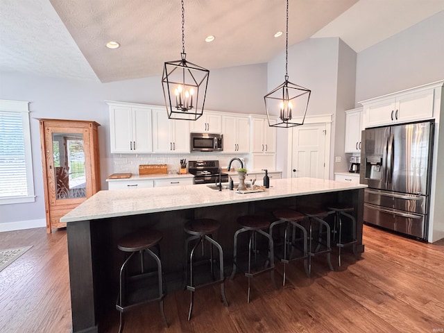 kitchen with appliances with stainless steel finishes, an inviting chandelier, a sink, decorative backsplash, and a spacious island