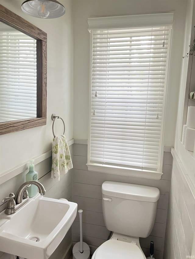 half bathroom with a sink, tile walls, wainscoting, and toilet